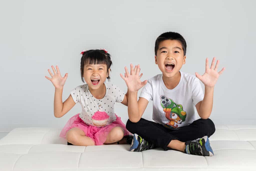 two Asian children laughing in studio with hands raised